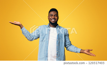 Make right choice. Handsome black man comparing variants, making scales with his empty hands over yellow studio background, panorama 120317403