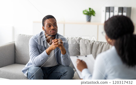 Psychological help service. Depressed black male patient having psychotherapy session with counselor at mental health clinic. Young man with emotional problems consulting professional therapist Psychological help service. Depressed black male patient having psychotherapy session with counselor at mental health clinic. Young man with emotional problems consulting professional therapist 120317432