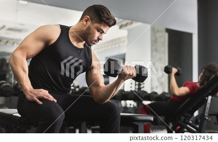 Arab muscular man doing biceps workouts with dumbbells in gym, copy space 120317434