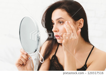 A woman is standing in front of a mirror, closely inspecting her reflection. She appears focused and thoughtful as she examines her features. 120317516