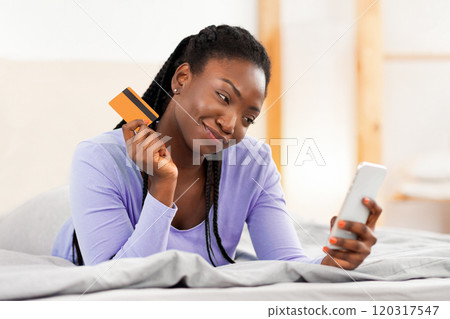 Mobile Shopping. African American Girl Holding Phone And Credit Card Lying In Bed At Home. Selective Focus 120317547