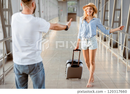 Meet And Greet Concept. Back view portrait of man greeting woman with open arms at the airport terminal Meet And Greet Concept. Back view portrait of man greeting woman with open arms at the airport terminal 120317660