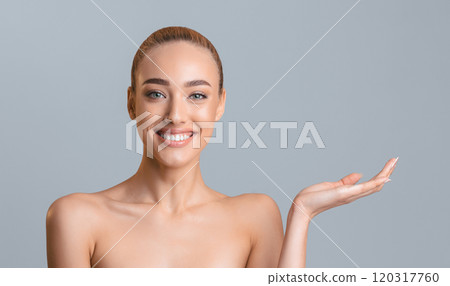 This image shows a young woman with long, straight brown hair, wearing no makeup, and smiling directly at the camera. She is posing with her right hand outstretched, palm up, copy space 120317760