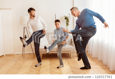 Happy Grandfather With Mature Son And Grandson Having Fun Pretending To Play A Guitar At Home. Multi-Generational Male Friendship 120317761