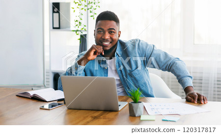 Portrait of young successful businessman sitting at his worplace in modern office and posing to camera, copy space Portrait of young successful businessman sitting at his worplace in modern office and posing to camera, copy space 120317817