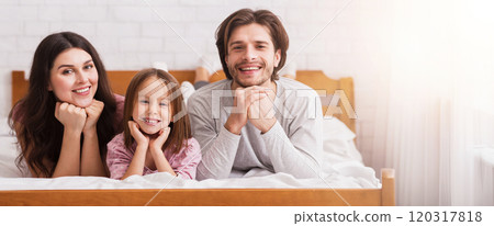 Portrait of happy family of three with little daughter posing on bed at home together and smiling to camera, free space Portrait of happy family of three with little daughter posing on bed at home together and smiling to camera, free space 120317818