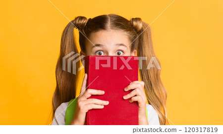 Back To School Anxiety. Scared Elementary Student Girl Hiding Behind Book On Yellow Studio Background. Free Space Back To School Anxiety. Scared Elementary Student Girl Hiding Behind Book On Yellow Studio Background. Free Space 120317819