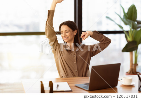 Get Rid Of Stiff Neck. Smiling young woman in brown long sleeve shirt stretching in front of desk at office, copyspace 120317831