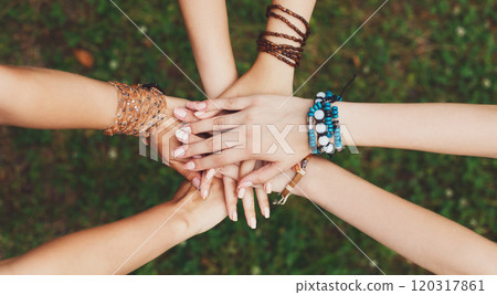 United hands of young females, top view. Stylish hands of girlfriends in boho hippie bracelets at green grass background. Togetherness and support, youth fashion and active lesiure. Women friendship 120317861