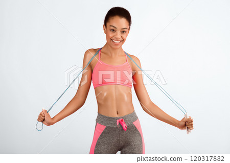 Fitness And Sport. Happy Millennial Girl In Fitwear Holding Jump Rope Standing Over Pink Studio Background. Fitness And Sport. Happy Millennial Girl In Fitwear Holding Jump Rope Standing Over Pink Studio Background. 120317882