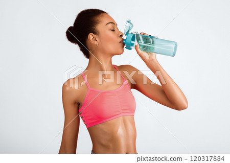 Sporty Black Woman Drinking Water From Bottle Standing Over Pink Background In Studio. Hydration And Workout Concept 120317884