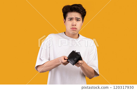 I'm Broke. Portrait of sad asian bankrupt showing his empty wallet and looking at camera. Upset crying male model standing isolated over orange studio background wall. Poverty Concept. I'm Broke. Portrait of sad asian bankrupt showing his empty wallet and looking at camera. Upset crying male model standing isolated over orange studio background wall. Poverty Concept. 120317930