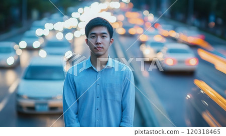 A young man stands still amidst the fast-moving traffic of a bustling city street during twilight 120318465
