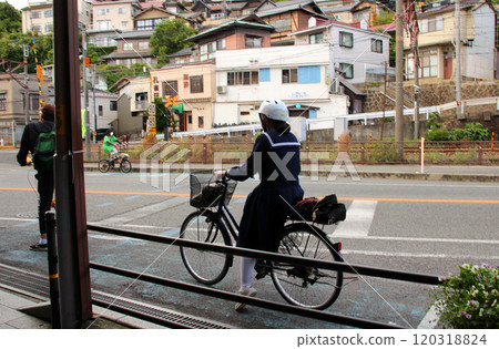 A high school girl wearing a helmet commuting to school by bicycle A high school girl wearing a helmet commuting to school by bicycle 120318824