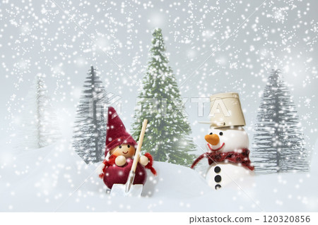 一個拿著鏟子的女孩和一個在飄落的雪中戴著水桶的雪人 120320856