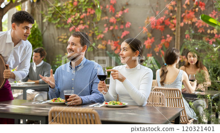 Waiter takes an order from a couple in love who decided to meet in an open air restaurant Waiter takes an order from a couple in love who decided to meet in an open air restaurant 120321401