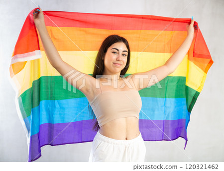Happy young woman with LGBT flag against unicoloured wall 120321462