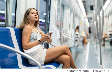 Young woman is sitting in subway car with headphones and phone, getting to work 120321594