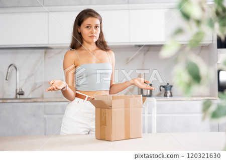 Young surprised woman holding open box in kitchen 120321630