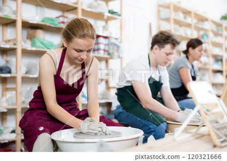 Young girl creates clay product on potter wheel in workshop 120321666