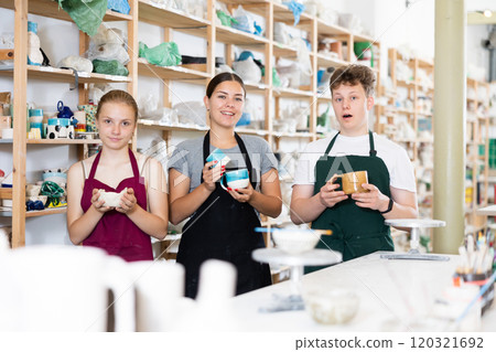 Young students, together with pottery teacher, show clay mugs they made with their own hands 120321692