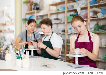 Young woman teacher helps teenagers boy and girl to sculpt ceramic product 120321791