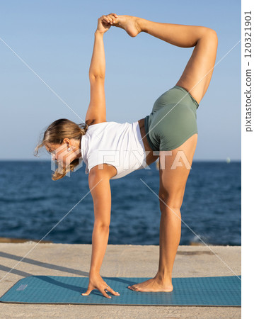 On windy day young slender woman does yoga near sea doing Natarajasana On windy day young slender woman does yoga near sea doing Natarajasana 120321901