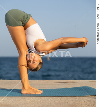 Sportive girl practicing forward bend pose of yoga on seashore 120321912