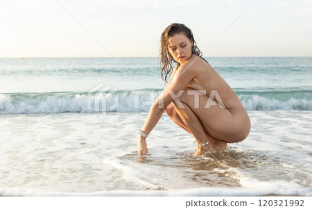 Young nude woman posing sitting on beach 120321992