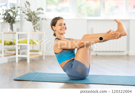 Sportive girl practicing boat pose of yoga in light room Sportive girl practicing boat pose of yoga in light room 120322004