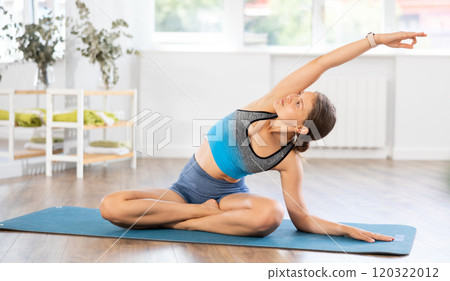Sportive girl practicing seated side bend pose of yoga in light room 120322012