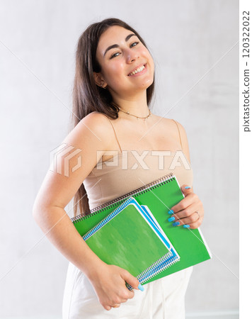 Young woman posing with notebooks against wall 120322022