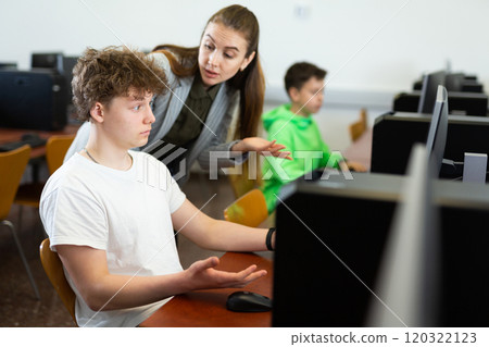 Female teacher consulting concentrated teenager in computer class 120322123