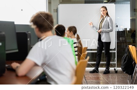 Teacher standing at marker board in computer class in front of pupils 120322149