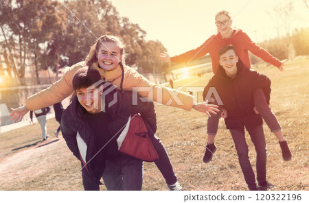 Cheerful teenage boys carrying girlfriends on back Cheerful teenage boys carrying girlfriends on back 120322196