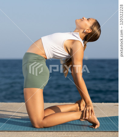 On windy day young slender woman does yoga near sea doing Ushtrasan 120322228