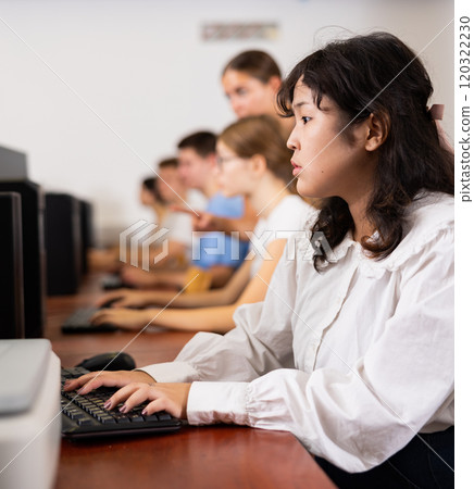 Portrait of fifteen-year-old schoolgirl studying at computer in class at an informatics lesson with classmates 120322230