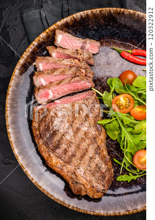 Grilled striploin steak, beef meat steak on a plate with salad. black background. top view 120322912