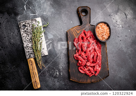 Uncooked Raw beef sliced meat, strips for cooking beef stroganoff on wooden board. black background. top view 120322924