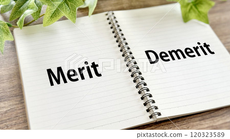 Open spiral notebook with the words Merit and Demerit written on it_Brown board background Open spiral notebook with the words Merit and Demerit written on it_Brown board background 120323589