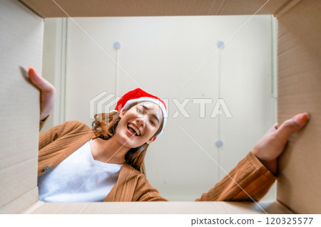 Low angle view of surprised young Asian woman wearing Christmas hat and unpacking 120325577