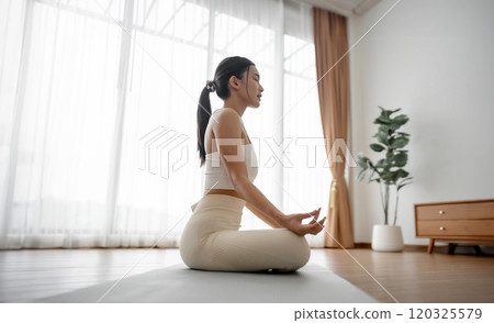 Young Asian woman meditating in lotus position at home Young Asian woman meditating in lotus position at home 120325579