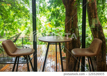 Cafe table and chairs by window with outdoor greenery garden Cafe table and chairs by window with outdoor greenery garden 120326935