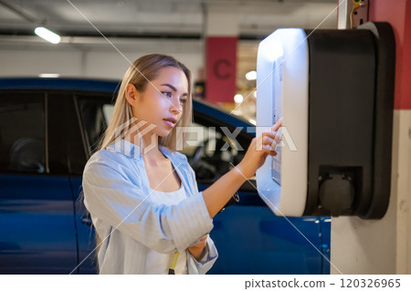 Woman initiates the charging process for her electric car in an indoor parking facility 120326965