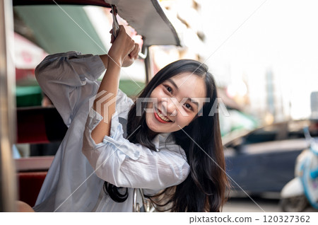 A beautiful Asian female tourist enjoying a ride in a tuk-tuk in Thailand, looking at the camera. 120327362