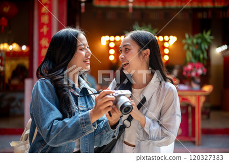 Two happy, pretty Asian female friends visit a Chinese shrine, checking photos on a camera together. Two happy, pretty Asian female friends visit a Chinese shrine, checking photos on a camera together. 120327383