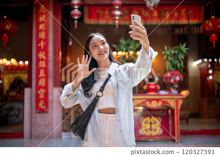 A happy Asian female tourist taking a selfie while visiting a stunning Chinese shrine. A happy Asian female tourist taking a selfie while visiting a stunning Chinese shrine. 120327391