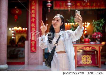 A happy Asian female tourist taking a selfie while visiting a stunning Chinese shrine. 120327392
