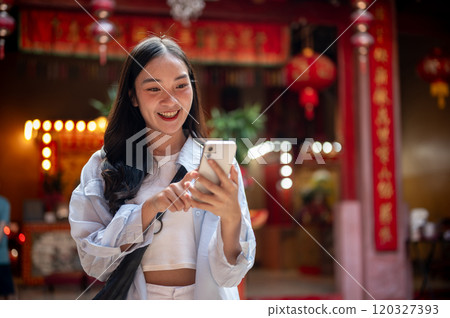 A smiling Asian female tourist using her smartphone while visiting a stunning Chinese shrine. 120327393