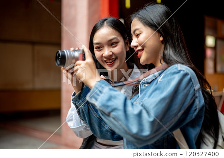 Cheerful Asian female friends check pictures on a camera together while visiting a Chinese shrine. Cheerful Asian female friends check pictures on a camera together while visiting a Chinese shrine. 120327400